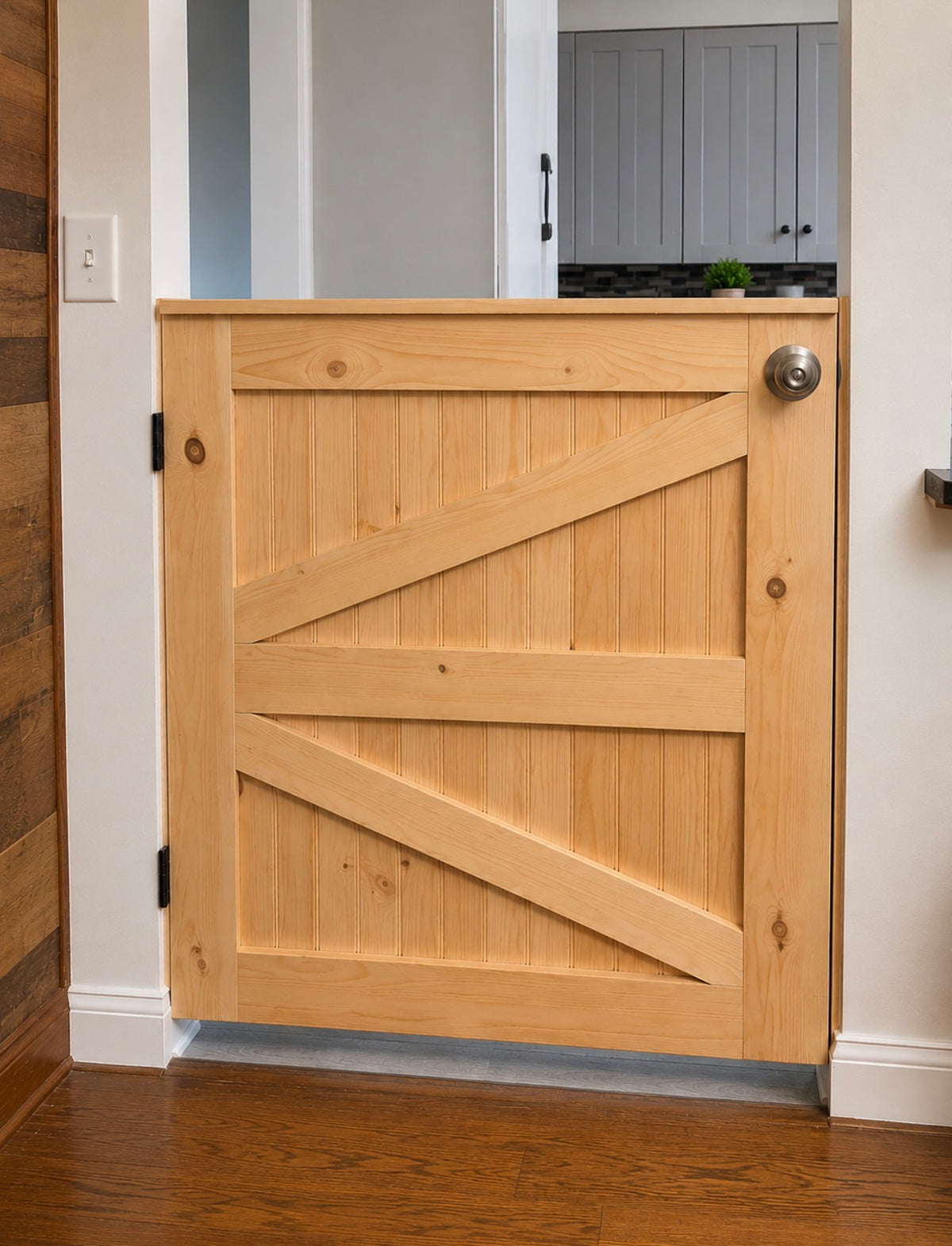 Custom natural wood K-frame gate installed in an interior doorway, featuring diagonal wood bracing, black hinges, and a silver doorknob.
